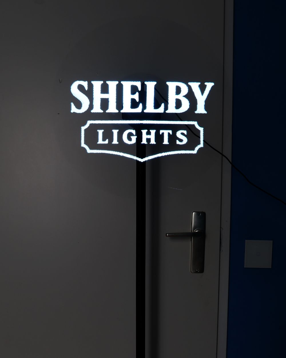 Het Shelby Lights-logo zweeft als 3D-hologram boven een zwarte standaard